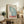 May include: Framed vintage-style poster featuring blue butterfly wing design with Japanese text and red "TOKYO" lettering, displayed on rustic wooden sideboard alongside fern plant, ceramic vases, and books in cozy living room setting with cream armchair and neutral walls.