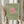 May include: Person holding framed art print featuring pink circle sun with black silhouette birds flying across sage green textured background, displayed with dried pampas grass in neutral beige interior setting with natural window light