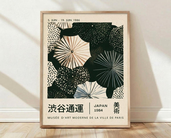 May include: Framed vintage Japanese exhibition poster featuring abstract umbrellas in cream, dark green, and muted blue with radiating spoke patterns and dotted textures. Text shows dates from 1986 and mentions Musée d'Art Moderne de la Ville de Paris. Light wood frame sits on wooden floor against white textured wall with soft shadows.