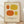 May include: Framed art print leaning against white wall on light wood floor. Cream-colored poster features four abstract oval shapes in orange and yellow tones - small orange oval top left, large yellow oval top right, large orange oval bottom left, small yellow oval bottom right. Black text at bottom reads "ELLSWORTH KELLY" and "Girande, 1964". Natural wood frame with soft shadows from window light creating diagonal patterns across the scene.