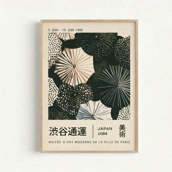Framed vintage exhibition poster featuring stylized umbrellas and fans in cream, dark green, and white with dotted patterns. Text shows dates "5. JUIN - 19. JUIN 1986" at top, Japanese characters, "JAPAN 1984," and "MUSÉE D'ART MODERNE DE LA VILLE DE PARIS" at bottom. Light wood frame against white wall background.