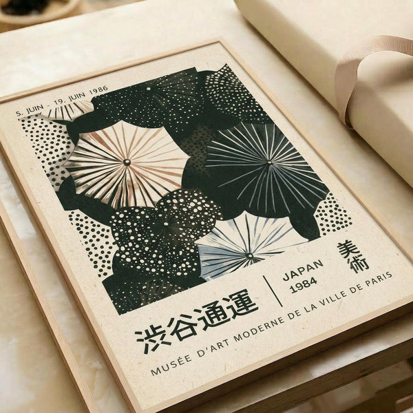 May include: Vintage-style poster with green silhouette shapes overlaying radiating umbrella designs in cream and sage tones, featuring Japanese and French text including "Japan 1984" and "Musee D'Art Moderne de la Ville de Paris." The print shows dotted pattern details and is displayed in a cream mat frame on neutral textured paper with soft lighting.