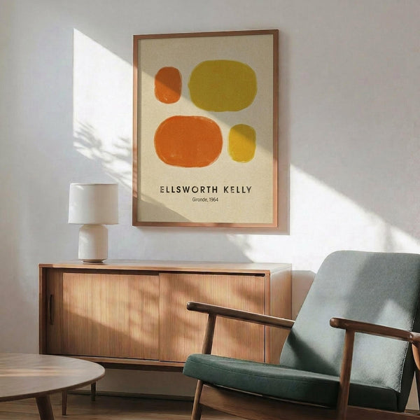 May include: Framed art print featuring four abstract oval shapes in orange, yellow, and olive green on cream background, displayed above mid-century modern wooden credenza with table lamp. Mint green upholstered chair with wooden arms sits nearby on hardwood floor. Sunlight creates geometric shadows on white wall in minimalist living room setting.