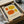 May include: Framed modern art print featuring four abstract organic shapes in orange and yellow tones on cream background, displayed in black frame inside cardboard packaging with protective wrapping, surrounded by shipping materials on white surface