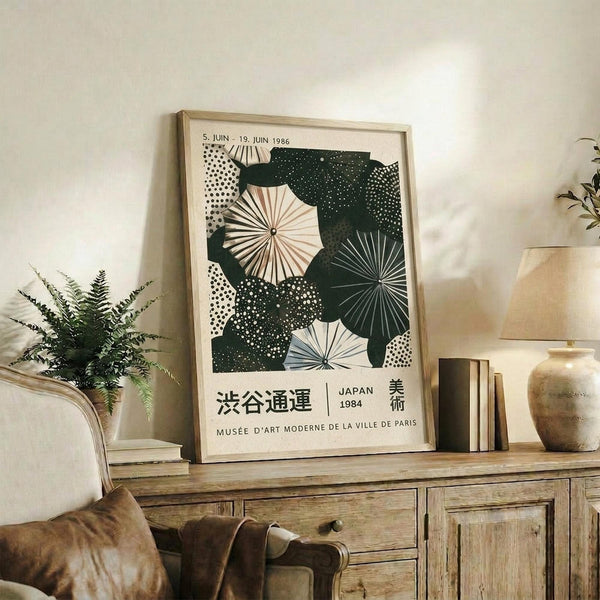May include: Framed vintage-style Japanese poster featuring green and white umbrella patterns with geometric designs and Japanese text, displayed on rustic wooden sideboard alongside books, ceramic vase, and small potted fern in neutral-toned living room setting with beige upholstered furniture.