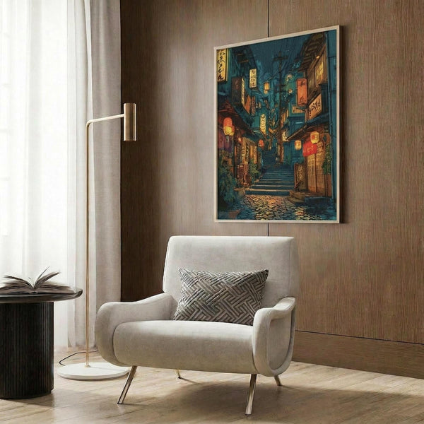 May include: Japanese street scene poster print with lantern-lit alley stairs in blue and orange tones, displayed in light wood frame on textured wood wall panel above cream upholstered armchair with geometric pillow, alongside brass floor lamp and black side table with open book in modern living room