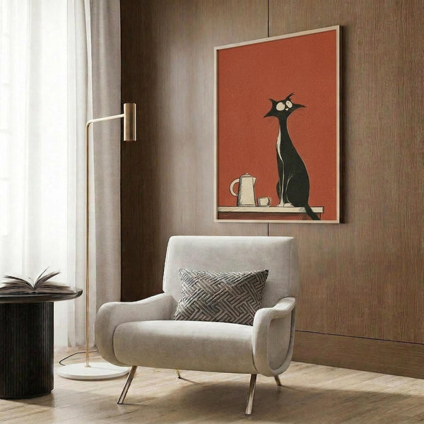 May include: Framed retro-style poster featuring black cat silhouette with white eyes sitting beside white coffee pot and cup on orange-red background, displayed on wood-paneled wall above beige upholstered armchair with geometric patterned pillow, alongside brass floor lamp and dark side table with open book in modern living room setting with neutral tones and natural lighting.