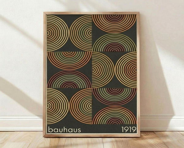 May include: Framed poster with geometric pattern of overlapping semicircular rainbow arcs in muted earth tones - greens, oranges, burgundy, and cream - on dark background. Text reads "bauhaus 1919" in white letters. Natural wood frame displayed on light wooden floor against white wall with soft shadows.