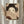 May include: Framed Japanese-style artwork showing a geisha with elaborate black hair adorned with cream flowers and dangling ornaments, holding a decorative fan that partially covers her face, displaying only her almond-shaped eyes and a red beauty mark on her cheek. The print features warm earth tones with intricate geometric patterns in the background. Displayed on a wall with dried pampas grass stems nearby and soft natural lighting from a window.