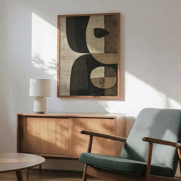 May include: Modern living room with sage green upholstered armchair, walnut sideboard, and white table lamp. Large framed abstract art print on white wall features geometric shapes in dark green, cream, and brown with textured, weathered appearance. Natural sunlight streams across the space, highlighting the mid-century modern furniture and warm wood tones throughout the room.