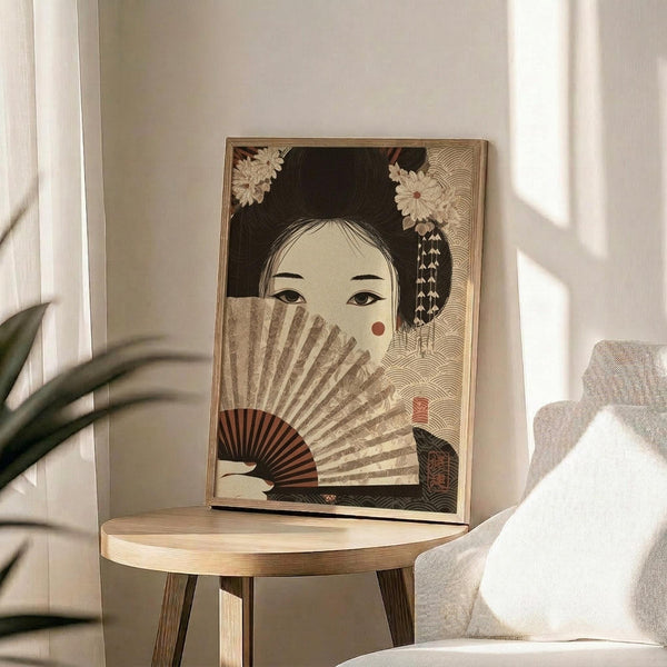 May include: Framed Japanese-style artwork displaying a geisha with black hair adorned with white flowers, holding an ornate fan that partially covers her face, set against a decorative wave pattern background. The print sits on a light wooden round side table next to a beige upholstered chair with white pillows, near a window with natural lighting and a potted plant visible in the corner.