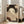 May include: Large framed poster leaning against white wall next to beige armchair in bright living room. Artwork shows Japanese woman with elaborate black hair adorned with flowers, holding decorative fan that partially covers her face. Muted earth tones with intricate wave patterns in background. Natural wood frame, approximately 3 feet tall.