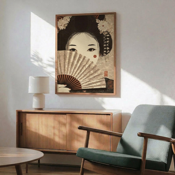 May include: Japanese-style artwork showing a woman with traditional hairstyle adorned with white flowers, holding an ornate folding fan that partially covers her face. The print features warm earth tones and intricate patterns, displayed in a wooden frame above a mid-century modern wooden credenza. A small white table lamp sits on the credenza next to a sage green upholstered armchair with wooden arms. Soft natural light creates dramatic shadows across the white wall.