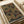 Vintage-style poster with geometric pattern of overlapping semi-circular arcs in warm earth tones including rust orange, olive green, burgundy, and cream on dark charcoal background. Text reads "bauhaus 1919" in white letters at bottom. Print has cream border and sits on light wood surface next to rolled white paper tube.