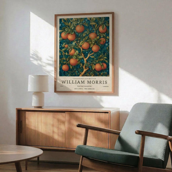 May include: Framed vintage-style exhibition poster featuring orange fruit tree with lush green foliage against deep blue background, displayed above mid-century modern wooden credenza with white ceramic lamp, next to sage green upholstered armchair with wooden frame in sunlit room with white walls.