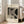 May include: A framed Bauhaus-style poster with geometric black and beige shapes and fine line patterns, displaying "BAUHAUS" and "Exhibition Art 1919" text. The cream-colored artwork sits against a light wood frame on hardwood floors beside a beige upholstered chair near bright windows in a minimalist white room.