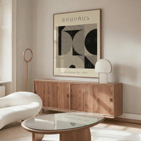 May include: Bauhaus-style poster with geometric black and beige shapes displayed above wooden sideboard in modern living room setting. White sculptural chair, glass coffee table, and minimalist table lamp complete the neutral-toned interior scene.