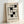 May include: Framed Bauhaus exhibition poster print leaning against white wall corner. Black geometric abstract design with interlocking rectangular shapes on cream textured background. Text reads "BAUHAUS EXHIBITION JULY 23, 1923" in black letters. Natural wood frame, minimalist modernist style artwork in bright indoor lighting.