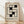 May include: Framed Bauhaus-style poster with geometric black squares forming an interlocking pattern on cream background, displayed in light wood frame against white textured wall on wooden floor with natural lighting casting diagonal shadows across the scene.
