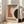 May include: Framed abstract geometric poster with orange, teal blue, cream and black curved shapes, featuring "BAUHAUS" text and "June 17, 1921" date. White frame leaning against wall next to beige upholstered chair in bright room with white curtains and hardwood floors.