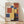 May include: Framed Bauhaus-style poster with geometric composition of overlapping colored rectangles in yellow, blue, red, and orange against cream background, displaying "BAUHAUS" and "1922" text, shown leaning against white wall on light wood floor with natural lighting casting shadows