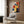 May include: Framed Bauhaus poster with colorful geometric shapes in red, yellow, blue, and orange displayed on wood paneled wall above beige upholstered armchair with patterned pillow. Modern brass floor lamp and side table with open book complete the minimalist living room scene with neutral tones and natural lighting.