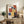 May include: Framed Bauhaus-style poster with geometric colorful rectangles in red, blue, yellow, and orange displayed on rustic wooden sideboard. Room scene shows neutral armchair, potted fern, ceramic vase, and books creating cozy living space with warm lighting and textured wall background.