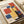 May include: Vintage Bauhaus exhibition poster from 1922 displayed in an open book or portfolio. The poster features geometric shapes in red, blue, and yellow colors arranged in an abstract composition against a cream background. The word "BAUHAUS" appears at the top with "1922" at the bottom. The book sits on a light wooden surface next to white ceramic objects, creating a minimalist styled scene.