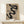 May include: Framed Bauhaus poster with black curved ribbons on beige textured background, displayed on light wooden shelf against white wall. Small white wrapped gift with twine sits nearby. Warm natural lighting creates soft shadows. Modern minimalist home decor styling with clean lines and neutral tones.