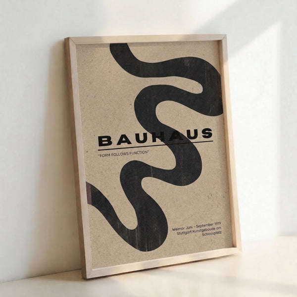 May include: Framed minimalist poster with black wavy serpentine design on beige textured background, featuring "BAUHAUS" text and "FORM FOLLOWS FUNCTION" motto, displayed against white wall corner. Natural wood frame with clean lines complements the modernist aesthetic. Poster shows historical details referencing Weimar and Stuttgart locations from 1919.