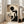May include: Framed Bauhaus-style geometric abstract poster with black circle, beige and brown rectangles, and vertical lines against cream background, displayed in light wooden frame leaning against white wall next to beige upholstered chair in bright, airy room with large windows