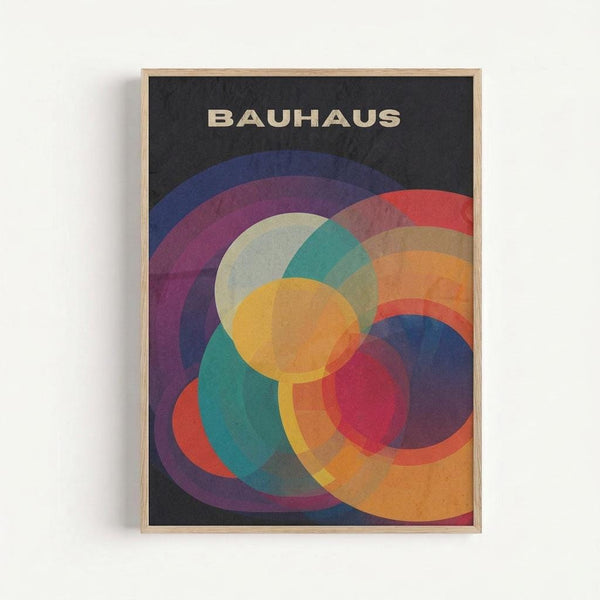 Framed poster with black background featuring overlapping translucent circles in vibrant colors including yellow, orange, red, purple, blue, teal, and green. The word "BAUHAUS" appears in beige letters at the top. The geometric design creates a dynamic flower-like pattern where circles intersect and blend colors. Natural wood frame against white wall background.