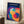 May include: Framed Bauhaus-style poster with overlapping translucent circles in vibrant blues, purples, yellows, oranges, and reds against dark navy background, white "BAUHAUS" text at top, displayed in modern living room setting leaning against white paneled wall beside beige armchair and wooden side table with coffee cup