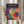 May include: Person holding framed Bauhaus-style poster with overlapping translucent circles in vibrant colors including blue, purple, red, orange, yellow, and teal against black background. Light wood frame, dried pampas grass visible, neutral beige clothing and curtains in soft natural lighting.