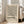 May include: Beige framed poster with black geometric line pattern and "BAUHAUS" text, leaning against white wall next to beige upholstered chair in bright room with large windows and light wooden floors