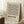 May include: Framed geometric poster with black linear zigzag pattern on beige background, displayed in bright room corner next to white coffee cup on wooden stool and cream textured blanket. Light wood frame casts soft shadows on white wall.