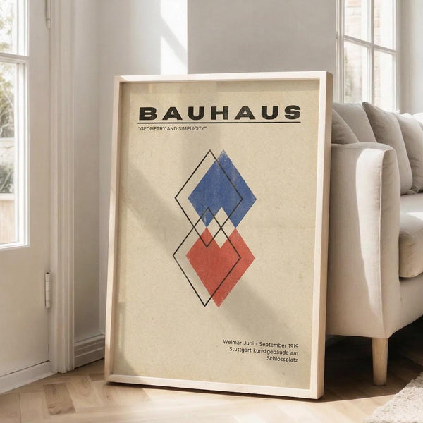 May include: Framed Bauhaus-style poster with geometric diamond shapes in blue and red on cream background, displayed on wooden floor next to beige sofa in bright living room with white walls and windows