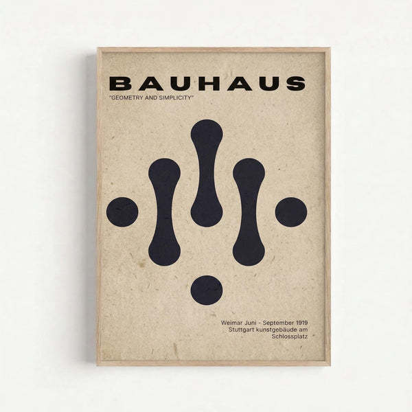 Framed Bauhaus-inspired poster with cream textured background featuring black geometric shapes arranged symmetrically - three elongated oval forms in the center flanked by two circles on each side, with a single circle below. Bold black "BAUHAUS" text at top with "GEOMETRY AND SIMPLICITY" subtitle. Small text at bottom references Weimar Juni-September 1919 Stuttgart kunstgebäude am Schlossplatz. Light wood frame against white wall background.