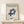 May include: Framed Bauhaus poster with blue geometric interlocking shapes and "LESS IS MORE" text displayed on light wood shelf against cream wall. Small wrapped gift box with twine and greenery sits beside the natural wood frame. Clean minimalist styling with soft natural lighting.