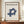 May include: Framed Bauhaus poster with "LESS IS MORE" text and blue geometric interlocking cube design on cream background, displayed on wooden sideboard with small ceramic vase and stacked books in elegant room with white wainscoting