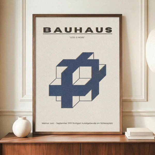 May include: Framed Bauhaus poster with "LESS IS MORE" text and blue geometric interlocking cube design on cream background, displayed on wooden sideboard with small ceramic vase and stacked books in elegant room with white wainscoting