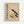 Framed Bauhaus-inspired poster with beige textured background featuring geometric shapes in yellow, dark green, and gray arranged diagonally. Bold black text reads "BAUHAUS MODERN ART" vertically on left side. German text appears at top and bottom describing the design school's history from 1919-1933. Minimalist composition with circles, rectangles, and striped patterns in modernist style, displayed in light wood frame against white wall.