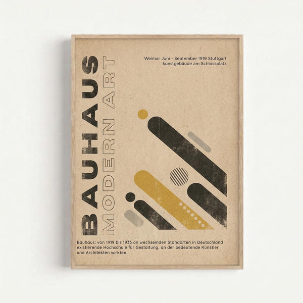 Framed Bauhaus-inspired poster with beige textured background featuring geometric shapes in yellow, dark green, and gray arranged diagonally. Bold black text reads "BAUHAUS MODERN ART" vertically on left side. German text appears at top and bottom describing the design school's history from 1919-1933. Minimalist composition with circles, rectangles, and striped patterns in modernist style, displayed in light wood frame against white wall.