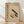 May include: Framed Bauhaus-inspired poster with geometric design featuring diagonal yellow and black bars, circles, and modern typography on beige background. Wood frame sits against white wall on light wooden floor with soft natural lighting creating shadows.