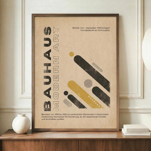 May include: Framed Bauhaus-inspired poster with beige background featuring geometric shapes in mustard yellow, dark green, and gray. German text reads "BAUHAUS MODERN ART" with exhibition details. Print displayed on wooden sideboard next to white ceramic vase and stacked books in modern interior with white paneled walls.