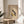 May include: Framed beige poster with "BAUHAUS MODERN ART" text and geometric shapes in black, yellow, and white displayed on light wood round side table next to cream upholstered chair. Sunlight streams through white curtains creating soft shadows. Green plant leaves visible in corner of minimalist room setting.