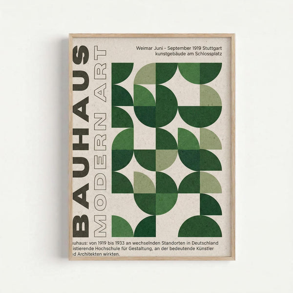 A framed poster with cream background featuring "BAUHAUS MODERN ART" in bold dark green letters on the left side. The right side displays a geometric pattern of overlapping green circles in various shades from light sage to deep forest green, arranged in a grid formation. German text appears at the top referencing Weimar 1919 Stuttgart, with additional German text at the bottom. The poster is displayed in a thin light wood frame against a white wall.