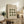 May include: Framed Bauhaus-style poster with green geometric circles arranged in a 3x3 grid pattern on beige background, displayed on rustic wooden sideboard alongside fern plant, books, ceramic vases, and brown leather chair in neutral-toned living room setting.