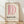 May include: Framed Bauhaus-style poster with pink curved shapes forming letter D on cream background, displayed in light wooden frame against white textured wall on wooden floor with soft natural lighting and shadows