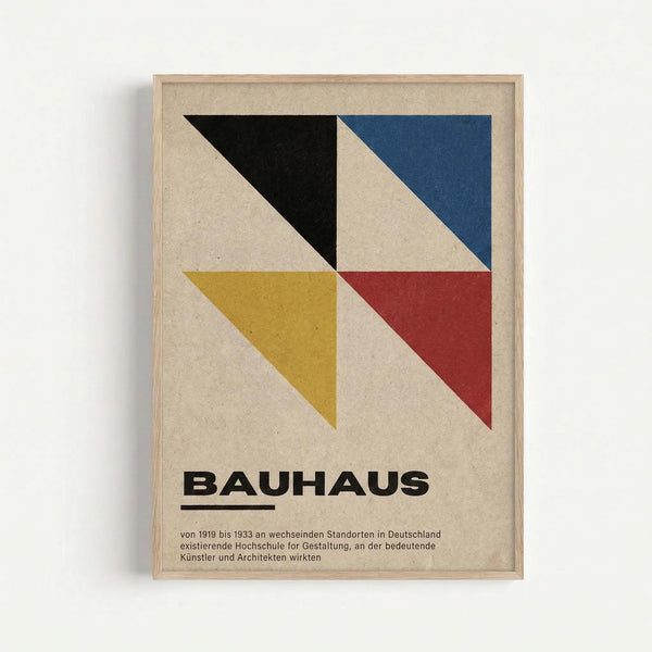 Framed geometric poster with four triangular sections in black, navy blue, mustard yellow, and burgundy red on beige textured background. Bold "BAUHAUS" text below the design with German descriptive text underneath. Light wood frame mounted on white wall.